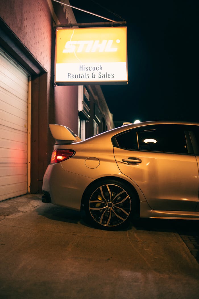 Night view of a car parked under an illuminated rental shop sign.